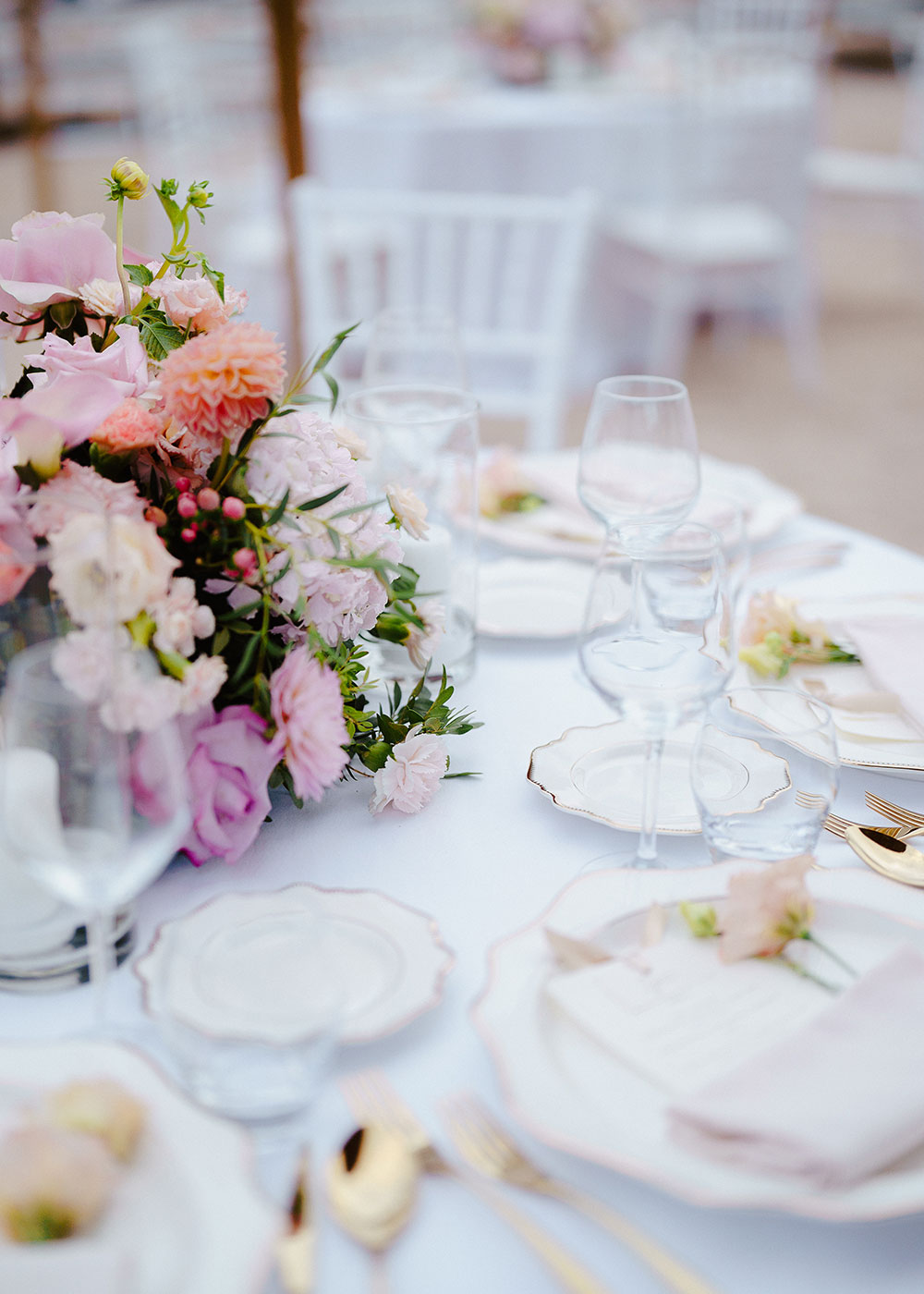 Mise en place elegante con piatti in porcellana, posate dorate e composizione floreale dai toni pastello