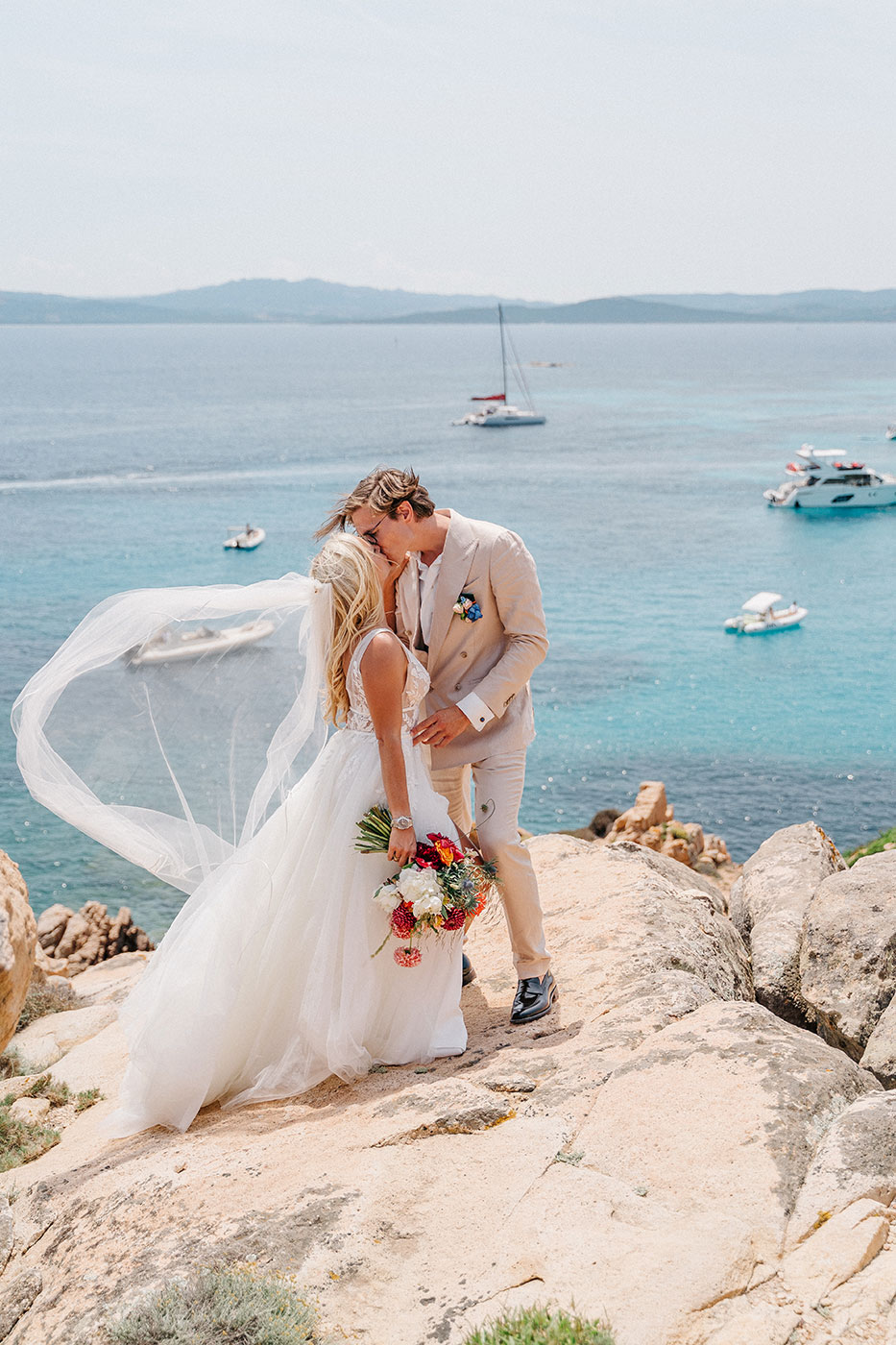 Sposi che si baciano sulle rocce affacciate sul mare cristallino della Sardegna