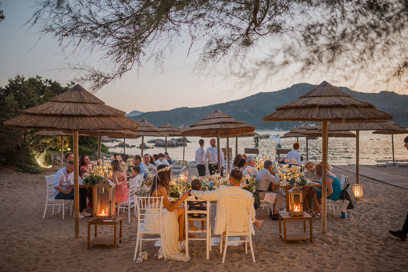 Ricevimento di matrimonio sulla spiaggia al tramonto con ospiti seduti a tavoli allestiti