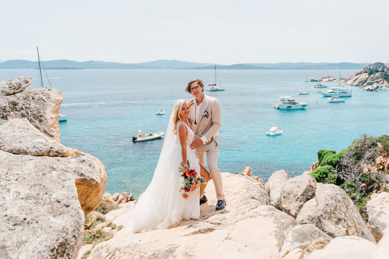 Gli sposi affacciati su una costa rocciosa con mare cristallino in Sardegna, scenario ideale per un destination wedding