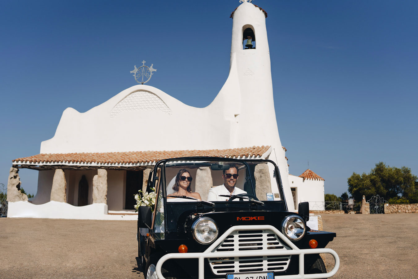 Gli sposi a bordo di un’auto vintage davanti a una chiesa in Sardegna, simbolo di un matrimonio elegante e senza tempo
